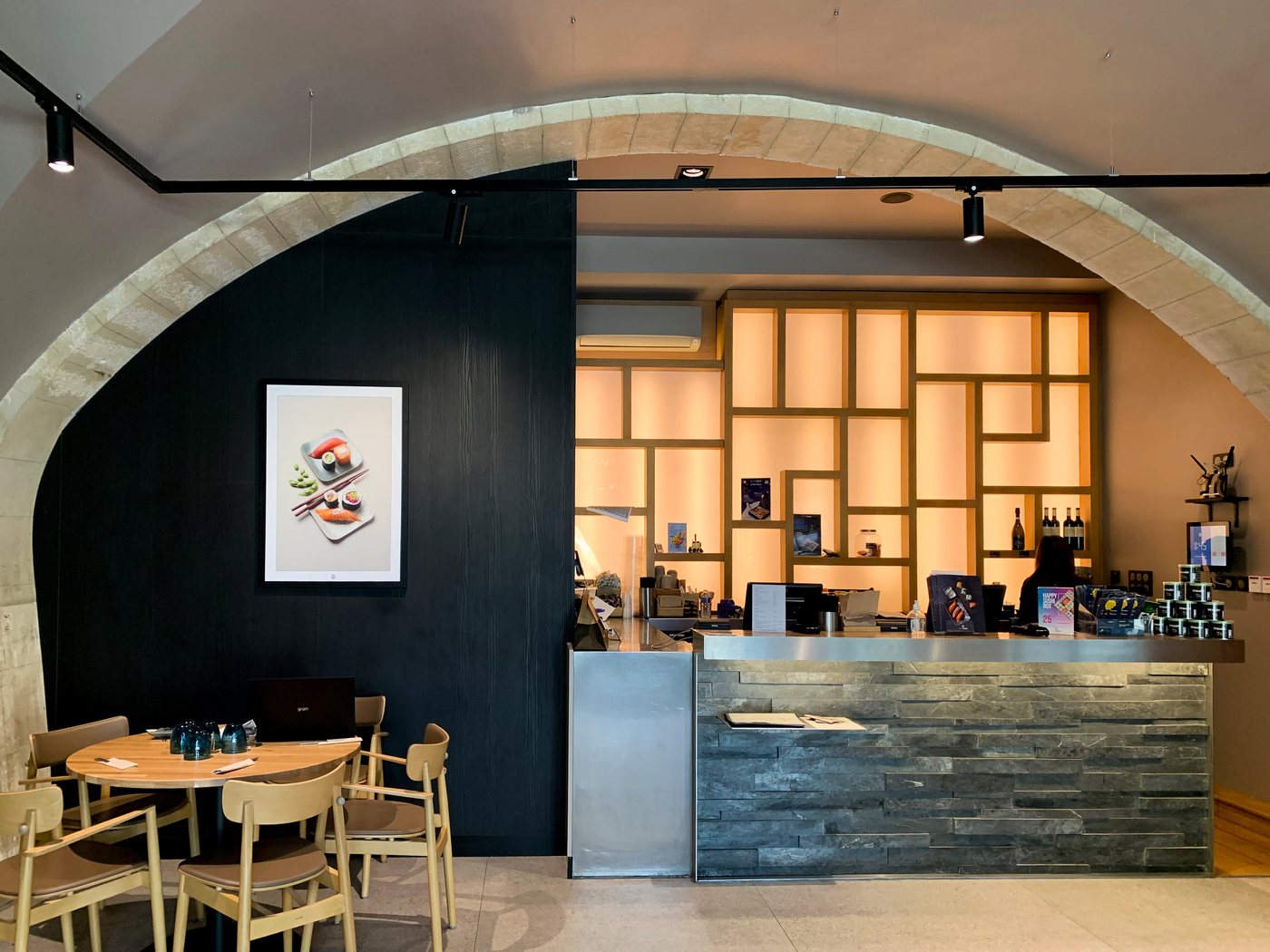 Sushi Shop Nîmes — stone vault over a black feature wall and backlit timber lattice behind the counter